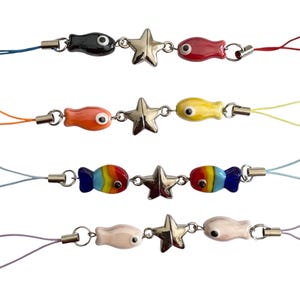 May include: A selection of colourful fish-shaped charms linked to star-shaped charms with silver-tone metal rings. Each charm is a different colour, including black, red, orange, yellow, rainbow, and white. Each charm has a matching coloured string.