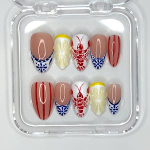 May include: A set of ten press-on nails in a clear plastic case. The nails feature various designs, including red and white lobster, yellow lemon, and blue floral patterns. Some nails have a nude base with red stripes or blue floral tips.