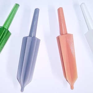 May include: Four pointed, multi-faceted tools arranged in a row. The first is translucent green, the second is opaque lavender, the third is opaque peach, and the fourth is translucent white. Each tool features a long, slender handle and a tapered body.