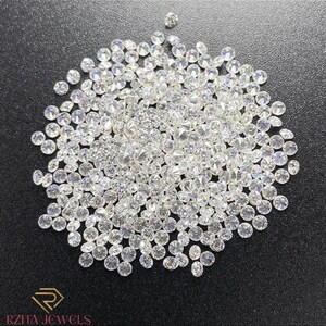 Pode incluir: Uma grande cole&ccedil;&atilde;o de diamantes redondos e brilhantes espalhados sobre uma superf&iacute;cie escura. Os diamantes s&atilde;o claros e refletem a luz, criando uma exibi&ccedil;&atilde;o brilhante. A imagem inclui o logotipo "RZITA JEWELS" em dourado.