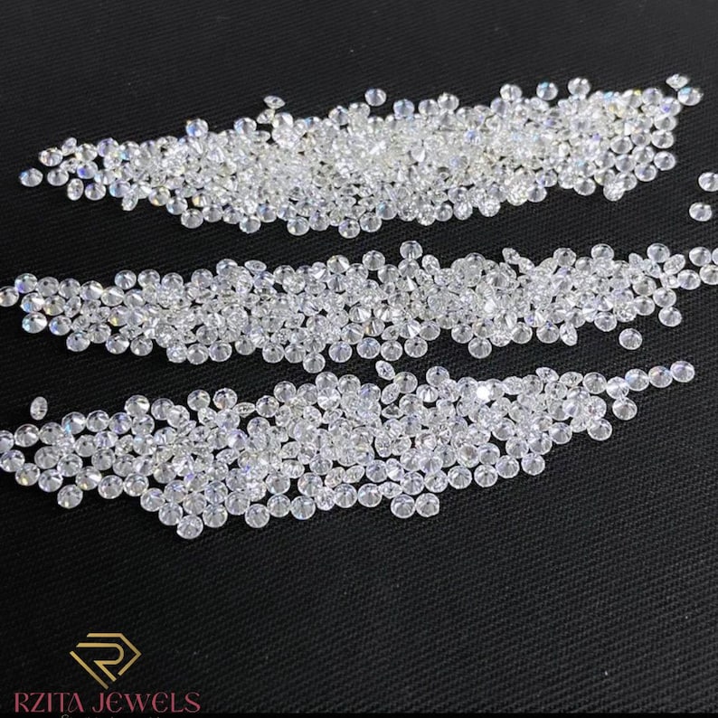Pode incluir: Uma cole&ccedil;&atilde;o de pequenos diamantes redondos e transparentes dispostos em tr&ecirc;s fileiras horizontais sobre um fundo preto. Os diamantes brilham, refletindo a luz. O logotipo "RZITA JEWELS" est&aacute; na parte inferior.