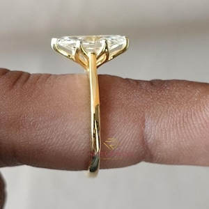 May include: A gold ring featuring a large, clear, pear-cut gemstone. The ring has a simple, polished gold band. The gemstone is secured by four prongs. The ring is viewed from the side.