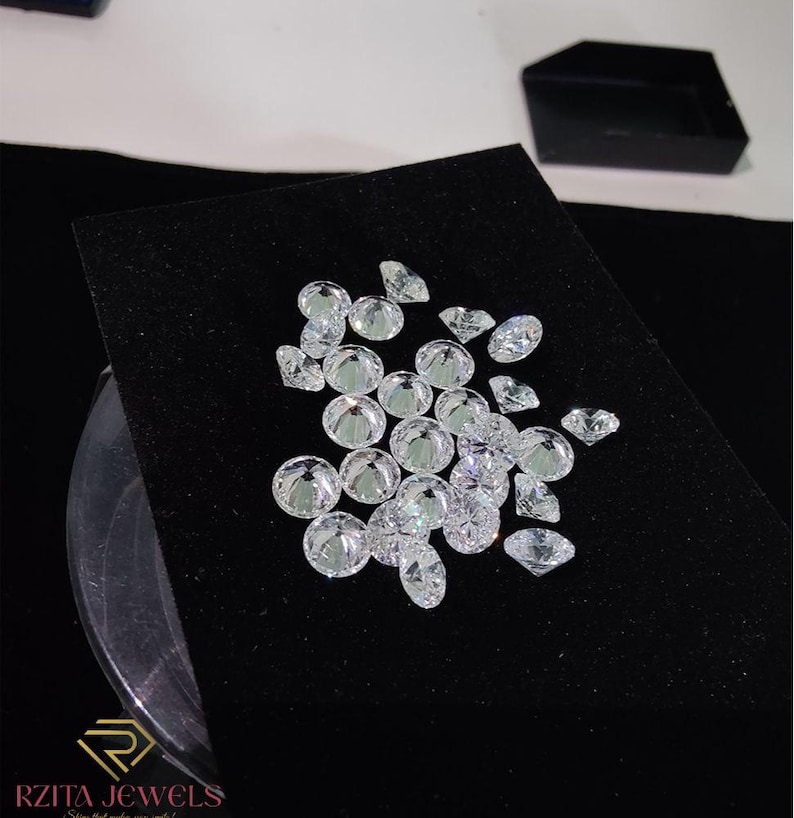 Pode incluir: Uma cole&ccedil;&atilde;o de diamantes claros e brilhantes de v&aacute;rias formas e tamanhos, incluindo cortes redondos e ovais, &eacute; exibida em uma superf&iacute;cie de veludo preto. Os diamantes refletem a luz, criando uma exibi&ccedil;&atilde;o brilhante. Uma caixa de joias preta est&aacute; no fundo.