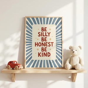 May include: A rectangular wall art print featuring a blue and white sunburst pattern with the text BE SILLY BE HONEST BE KIND in dark red letters, centered on a cream background with small star and flower icons, displayed on a wooden shelf.