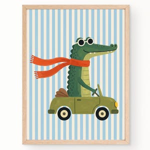 May include: A framed wall art print featuring a green crocodile wearing white-rimmed sunglasses and a long orange scarf, driving a small olive green convertible car. The background consists of vertical light blue and white stripes.