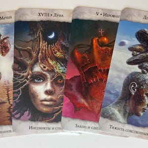 Op de afbeelding: Vier tarotkaarten met gedetailleerde illustraties. De kaarten bevatten afbeeldingen van een menselijke figuur, een hart, een gezicht met boomachtig haar en een figuur met stenen boven hun hoofd. Elke kaart heeft tekst in een vreemde taal.
