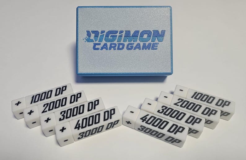 May include: A set of white plastic counters with black text for the Digimon Card Game. The counters are labeled with plus and minus signs and different point values: 1000, 2000, 3000, and 4000.