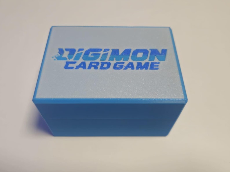 May include: A blue box with a white top and the text "Digimon Card Game" printed on it.