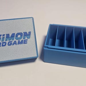 May include: A blue plastic storage box with a hinged lid. The box has six compartments and is labeled "Digimon Card Game".