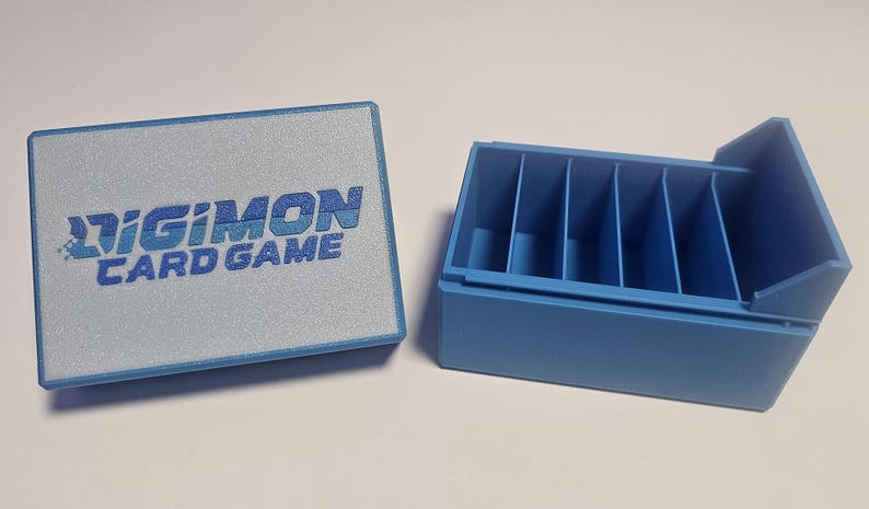 May include: A blue plastic storage box with a hinged lid. The box has six compartments and is labeled "Digimon Card Game".