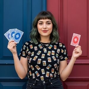 May include: A black t-shirt with tarot card illustrations. The person in the image is holding playing cards with blue and red backs. The background is a blue and red door.