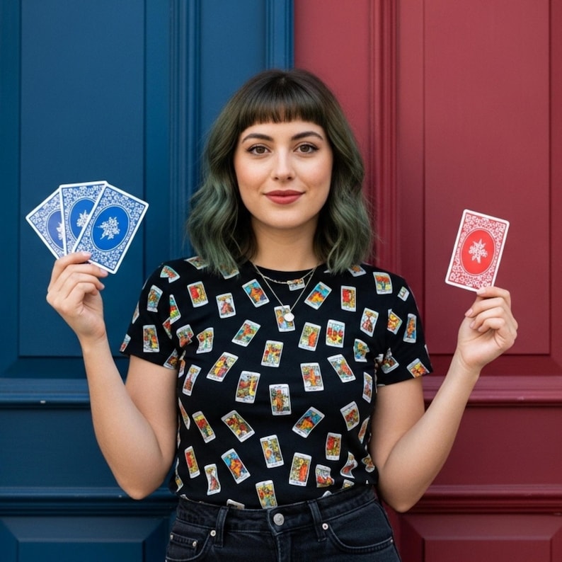 May include: A black t-shirt with tarot card illustrations. The person in the image is holding playing cards with blue and red backs. The background is a blue and red door.