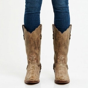 May include: A pair of brown leather cowboy boots with a snakeskin pattern on the foot and lower leg. The boots have a scalloped top and are worn with blue jeans.