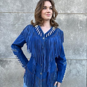 May include: A blue suede jacket with long fringe detailing. The jacket features white stitching accents on the collar, sleeves, and button placket. The jacket is buttoned up and has a classic Western style.