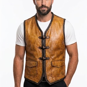 Puede incluir: Un chaleco de cuero marr&oacute;n con cuello en V, dos bolsillos delanteros y tres cierres de hebilla. El chaleco tiene un ribete trenzado marr&oacute;n oscuro y se usa sobre una camiseta blanca. El cuero parece envejecido.