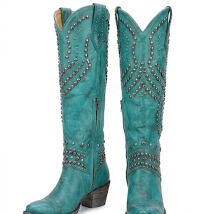 Könnte beinhalten: Ein Paar kniehohe, blaugrüne Stiefel mit Used-Optik, spitzer Zehenpartie und Blockabsätzen. Die Stiefel sind mit komplexen Mustern aus silberfarbenen Metallnieten und kleinen türkisfarbenen Akzenten am Schaft und Knöchel verziert.