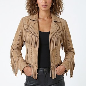 Könnte beinhalten: Hellbraune Wildlederjacke mit Fransen an Ärmeln, Brust und Rücken. Die Jacke hat einen Reverskragen, einen Reißverschluss und dekorative Nähte. Das Model trägt ein schwarzes Top und eine schwarze Lederhose.