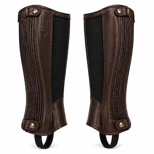 May include: A pair of dark brown leather half chaps featuring vertical pleated detailing, black elastic side panels, and brass-toned snap button closures at the top and bottom. Each chap includes a black elastic stirrup strap at the base.