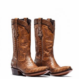 Può includere: Un paio di stivali da cowboy in pelle marrone. Gli stivali presentano intricati disegni in rilievo, tra cui motivi floreali e a volute, e un motivo strutturato simile a quello di un alligatore sul piede e sullo stelo superiore. Hanno punte a punta e tacchi impilati.
