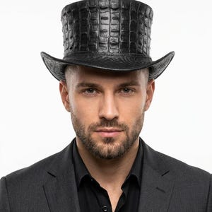 May include: A black top hat with a textured, crocodile-like pattern. The hat has a wide brim and a tall, cylindrical crown. The hat is worn with a black shirt and a dark grey suit jacket.