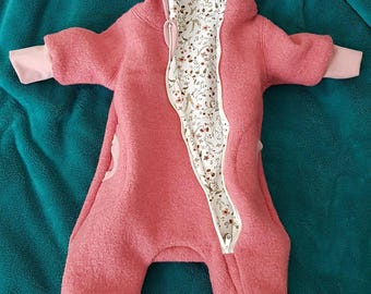 Peut inclure: Combinaison rose pour bébé avec capuche et fermeture éclair intégrale. L'intérieur de la capuche et la doublure de la fermeture éclair présentent un motif floral. La combinaison a des pieds et des manches avec des poignets rose clair. Le vêtement est en matière douce et moelleuse.