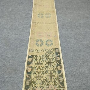 May include: A long, rectangular rug with a beige background and floral and geometric patterns in shades of blue, green, and pink. The rug has a distressed, vintage look, with a fringed edge. The rug is approximately 10 feet long.