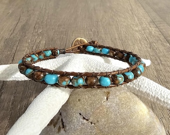 May include: A wrap bracelet featuring alternating round turquoise-colored beads and brown mottled beads strung on dark brown leather cord. The bracelet is secured with a circular metal button closure, creating a double-strand appearance.