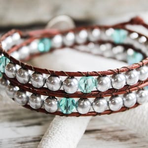 May include: A brown leather wrap bracelet with silver and turquoise beads. The bracelet is double-wrapped and has a simple closure.