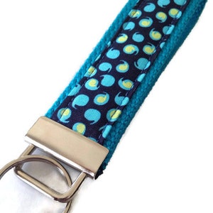 May include: A teal blue key chain with a navy blue fabric strap featuring a white and teal polka dot pattern. The key chain has a silver metal ring.