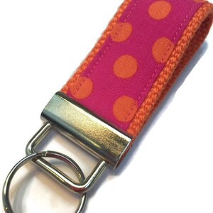 May include: A pink and orange polka dot key chain with a silver key ring.