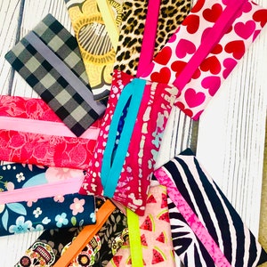 May include: Assortment of colorful fabric tissue holders with various patterns, including hearts, animal print, watermelon, and skulls. Each holder has a zipper closure and a contrasting fabric strip.