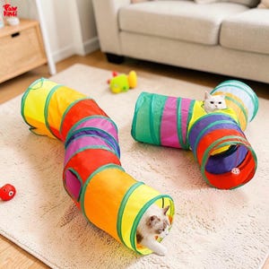Puede incluir: Dos túneles coloridos para gatos en un salón. Un túnel es curvo y el otro es recto. Un gato blanco está dentro del túnel recto, y otro gato está en el túnel curvo. Los túneles están hechos de tela de colores del arcoíris.
