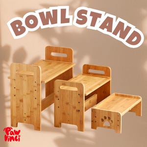 May include: Four bamboo pet bowl stands in different sizes. The stands have a natural wood finish and a rectangular top with a handle or paw print detail. The text "BOWL STAND" is displayed above the stands.
