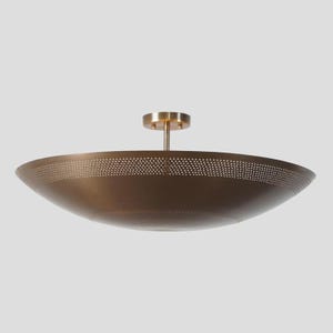 Könnte beinhalten: Eine schüsselförmige Deckenleuchte mit metallischem Bronzefinish. Der breite, flache Schirm weist am oberen Rand ein Band aus kleinen, gleichmäßig verteilten Perforationen auf und ist an einer zentralen zylindrischen Halterung befestigt.