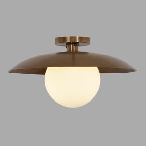 May include: A brass ceiling light fixture with a round, white glass shade. The fixture has a flat, circular base and a curved, upward-facing shade.
