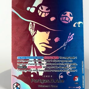 May include: A holographic trading card featuring Portgas D. Ace from the Whitebeard Pirates. The card has a blue and red color scheme with the character's image and game text. The card has a power level of 6000 and a life value of 3.