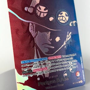May include: Holographic trading card featuring Portgas D. Ace from the Whitebeard Pirates. The card has a 6000 base power and includes game text. The card's background is a mix of red and blue with a portrait of Ace.