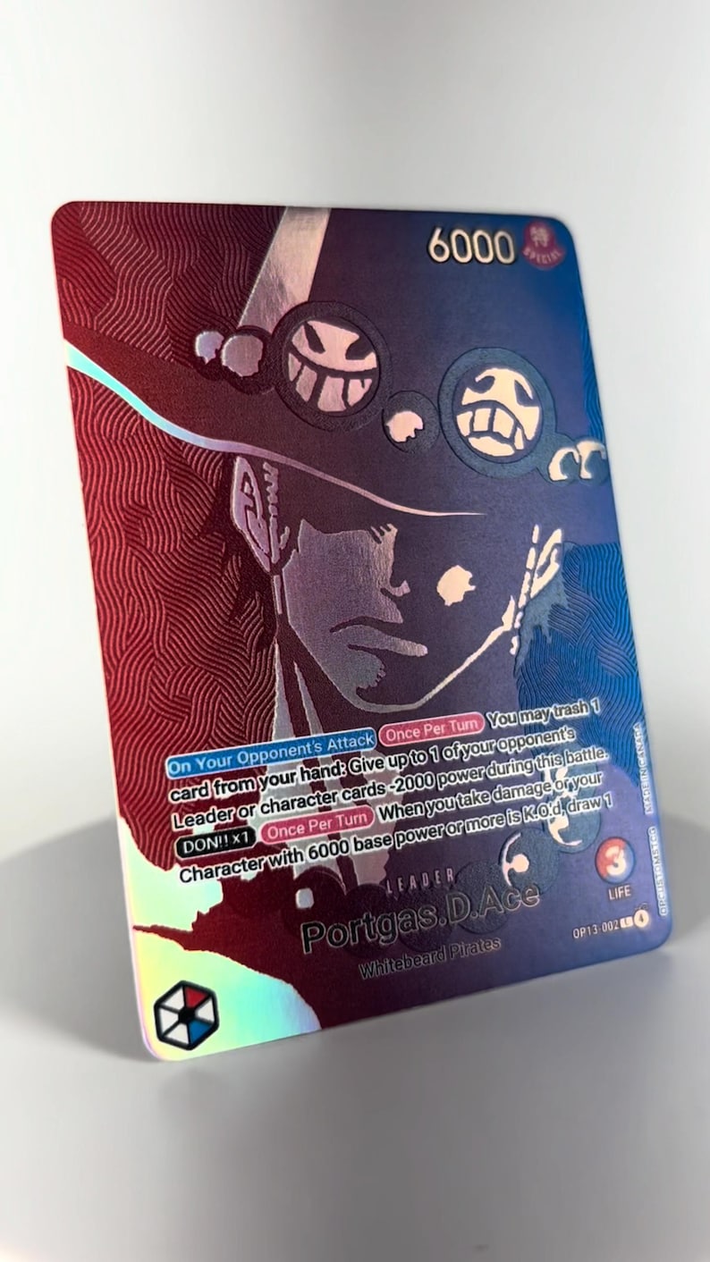 May include: Holographic trading card featuring Portgas D. Ace from the Whitebeard Pirates. The card has a 6000 base power and includes game text. The card's background is a mix of red and blue with a portrait of Ace.