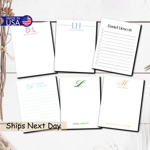 May include: A collection of personalized notepads with various designs. Each notepad features a different initial or name, with options for lined or checklist formats. The notepads are white with text in pink, blue, green, and gold. The image includes a "Made in USA" sticker.