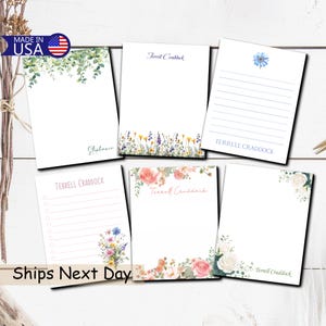 May include: A collection of white notepads with floral and botanical designs. Some pads feature lines, while others have a blank space for writing. The pads are adorned with various floral arrangements, including roses, wildflowers, and greenery. The text "Terrell Craddock" and "Stephanie" are printed on some pads.