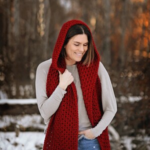 Puede incluir: Una mujer con una bufanda de capucha de ganchillo roja en un entorno de bosque nevado.