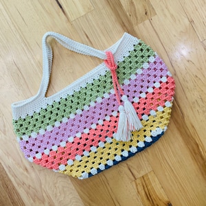 May include: A multi-colored crocheted tote bag with a white tassel. The bag is made with a granny square stitch and features stripes of green, pink, orange, yellow, and blue.
