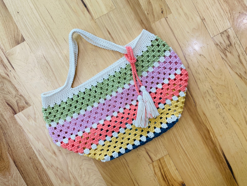 May include: A multi-colored crocheted tote bag with a white tassel. The bag is made with a granny square stitch and features stripes of green, pink, orange, yellow, and blue.