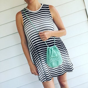 May include: A woman wearing a black and white striped sleeveless dress with a light green crocheted drawstring bag with a tassel.