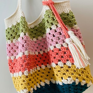 May include: A colorful crocheted tote bag with a white tassel. The bag is made with different colored yarn in stripes of green, pink, orange, yellow, and blue.