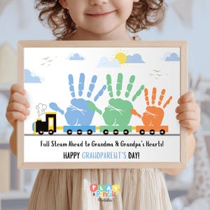 May include: A framed print with a train design made of handprints in blue, green, and orange. The text reads "Full Steam Ahead to Grandma & Grandpa's Hearts! HAPPY GRANDPARENT'S DAY!" against a white background with a sun and clouds.