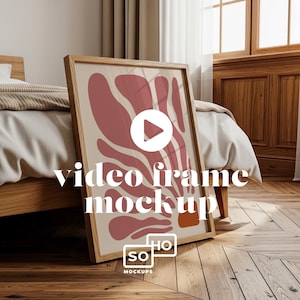 Könnte beinhalten: Ein gerahmter Kunstdruck mit hellem Holzrahmen, der ein modernes abstraktes Design in Rosa- und Beigetönen zeigt. Die Worte "video frame mockup" sind auf dem Druck abgebildet. Der Rahmen lehnt an einem Bett in einem Schlafzimmer.