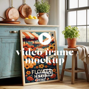 Puede incluir: Una impresión artística enmarcada que presenta una vibrante escena de mercado de flores con toldos a rayas naranjas y blancas, girasoles y rosas. La impresión se muestra en un marco de madera clara, apoyada contra un gabinete azul. El texto "video frame mockup" es visible.
