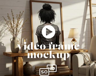Op de afbeelding: Een ingelijste kunstdruk met een vrouw met krullend haar, gekleed in een gestreept shirt, die wegkijkt. Het frame staat op een rustieke houten console met een lamp, vaas en boeken. De tekst "video frame mockup" is over de afbeelding geplaatst.