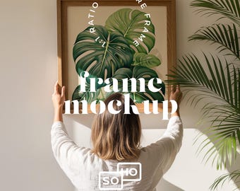 Op de afbeelding: Een vierkante houten frame-mockup met een verhouding van 1:1, met een aquarel schilderij van grote groene monstera bladeren. Het frame wordt door een persoon omhoog gehouden. De tekst "frame mockup" wordt in het wit weergegeven.